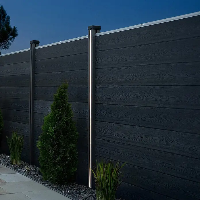 HOME DELUXE Nutleiste mit Solar LED Beleuchtung CALLUX STRIPE - 1er Set -  - Dunkelgrauer WPC-Zaun mit integrierter LED-Beleuchtung in den Pfosten, im Dämmerlicht mit kleinen Pflanzen.