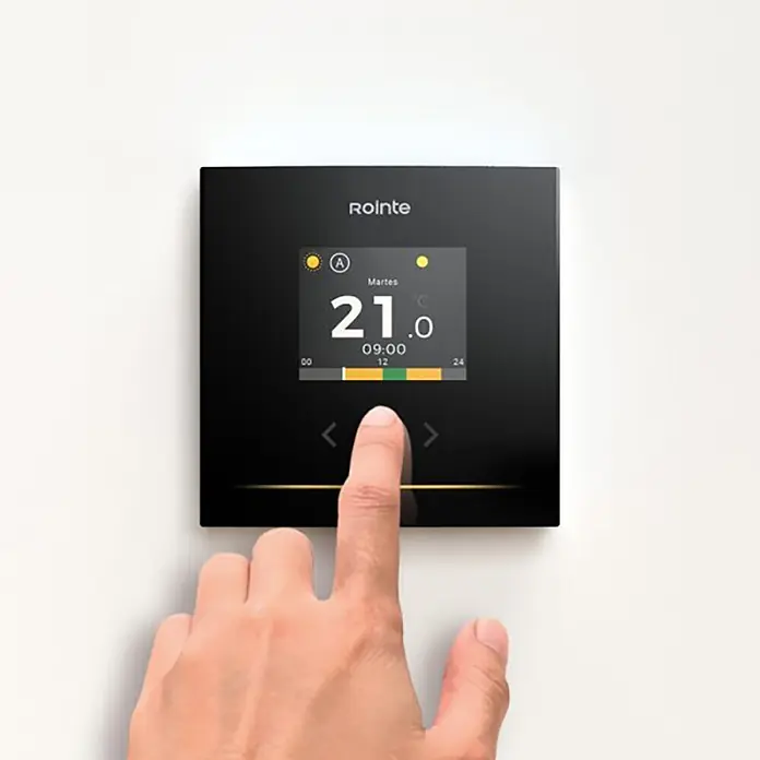 Termostato digital Genius - An x Al: 8,6 x 8,6 cm, Negro - Un termostato inteligente negro con pantalla digital que muestra 21,0°C y 09:00. Una mano toca la pantalla interactiva.