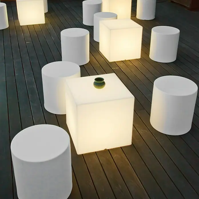 New Garden Design-Außenleuchte Cuby 3232 x 32 x 32 cm, Warmweiß - Beleuchtete Sitzgruppe mit weißen, zylindrischen Hockern und quadratischen Tischen, die eine moderne und stilvolle Atmosphäre schaffen.