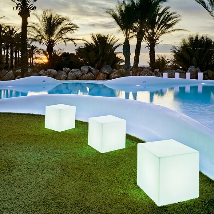 New Garden Design-Außenleuchte Cuby 45 - 45 x 45 x 45 cm, Warmweiß - Außenaufnahme mit drei beleuchteten Würfeln auf Gras, Pool im Hintergrund.