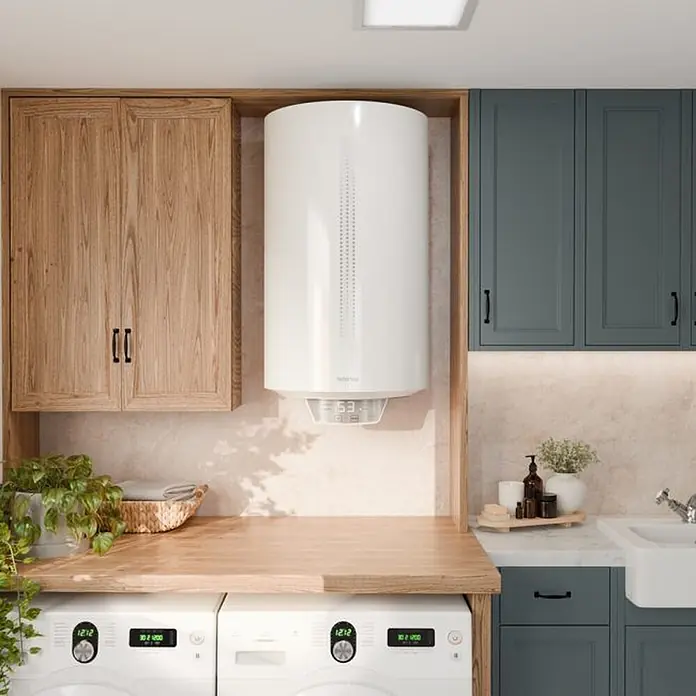 Rointe Termo eléctrico Evia - 100 l, 1.500 W - Un elegante calentador de agua cilíndrico blanco está montado entre gabinetes de madera y verde oscuro en una lavandería moderna.