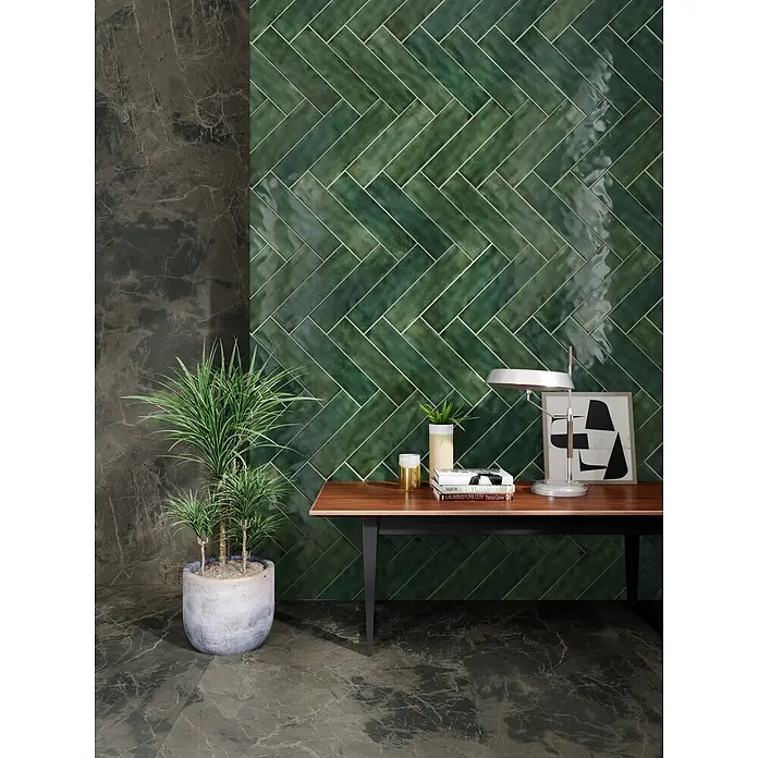 Wandfliese JULIET VERT – 7.5 x 30 cm, Zellige-Optik, Brillant -  - Grüne glänzende Keramik-Metrofliesen im Fischgrätmuster an der Wand, mit dunklem Marmorboden und Dekoration in einem modernen Raum.