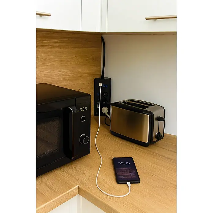 Base de enchufe múltiple Corner 4 - Negro, Longitud del cable: 1,5 m, Con interruptor - Regleta negra en encimera de cocina, alimentando microondas, tostadora y cargando un smartphone.