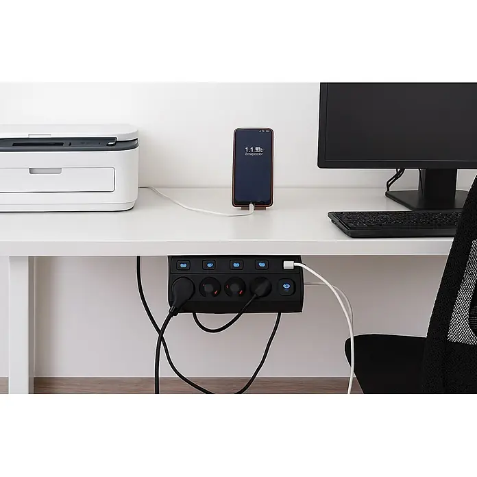Base de enchufe múltiple Corner 4 - Negro, Longitud del cable: 1,5 m, Con interruptor - Regleta negra con múltiples tomas y puertos USB, montada bajo un escritorio, organizando cables para un teléfono, impresora y monitor.