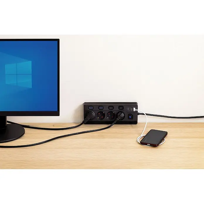 Base de enchufe múltiple Corner 4 - Negro, Longitud del cable: 1,5 m, Con interruptor - Regleta negra con tomas AC y puertos USB en un escritorio de madera, alimenta un monitor y carga un teléfono.
