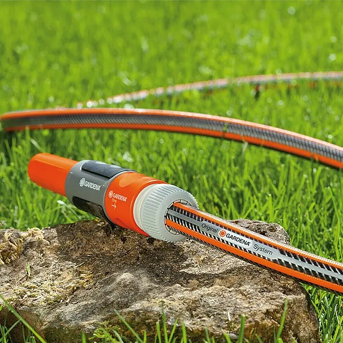 Gardena Schlauch Premium SuperFlex - Länge: 50 m, Schlauchdurchmesser: 13 mm, 35 bar - Nahaufnahme eines Gardena-Schlauchstücks auf einem Stein. Das orange-graue Kunststoffteil ist an einen Gartenschlauch mit der Aufschrift "Gardena System" befestigt.