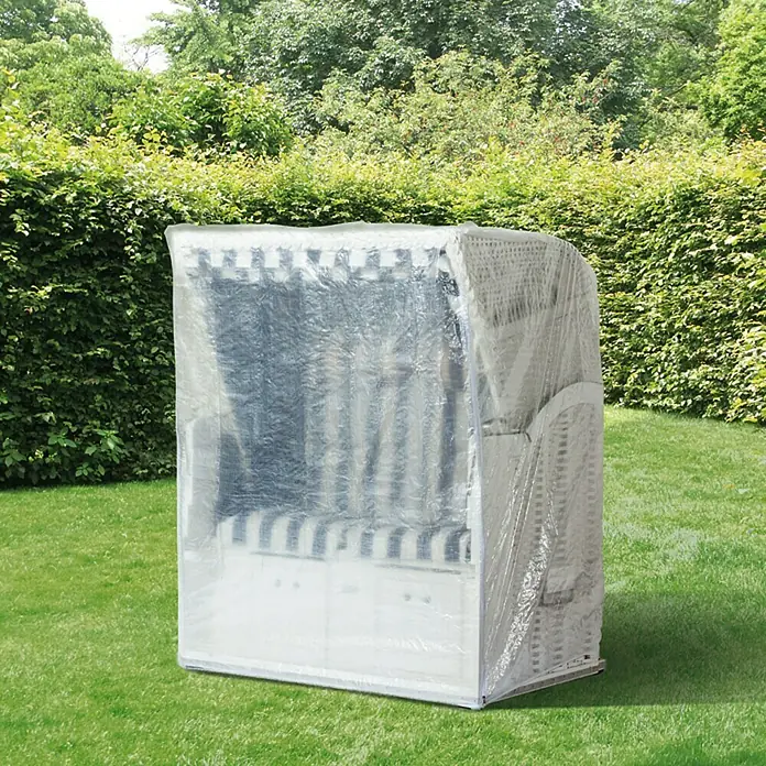 Sunfun Classic Strandkorb-Schutzhülle - L x B x H: 130 x 100 x 170 cm, PE-Bändchengarn, 90 g/m², Transparent - Ein Strandkorb mit einer durchsichtigen Schutzhülle steht auf einer Rasenfläche und ist von Büschen umgeben.