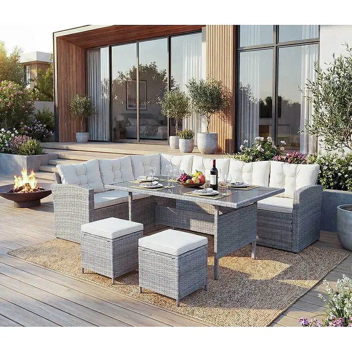 Mendler Loungemöbel-Set HWC-A29 - 5 -tlg., Polyrattan, Hellgrau, Kissen creme + 2x Hocker, Hellgrau - Graue Rattan-Outdoor-Eckessgruppe mit weißen Kissen, Glastisch und zwei Hockern auf einer Terrasse.