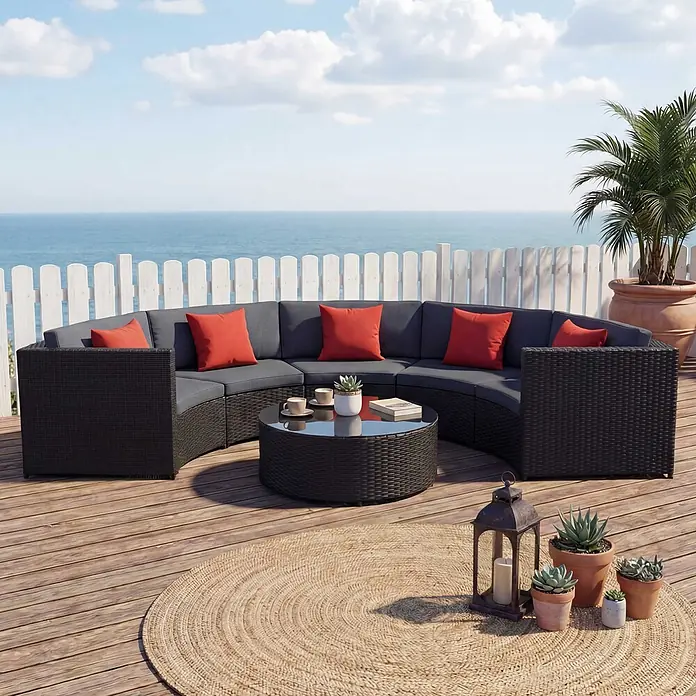 Mendler Loungemöbel-Set HWC-E17 - 6 -tlg., Polyrattan, Schwarz, Polster dunkelgrau, Kissen terracotta, Schwarz, dunkelgrau - Dunkelbraunes geschwungenes Outdoor-Rattan-Sofa-Set mit grauen Kissen, roten Kissen und einem runden Couchtisch auf einer Holzterrasse am Meer.
