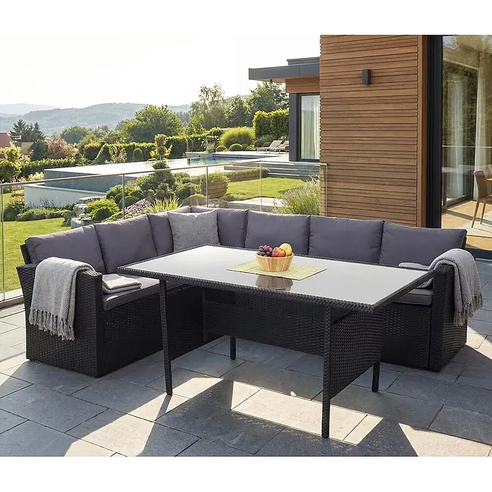 Mendler Loungemöbel-Set HWC-A29 - 2 -tlg., Polyrattan, Kissen dunkelgrau, Schwarz, dunkelgrau - Schwarze Rattan-Eck-Gartengarnitur mit grauen Kissen und Glastischplatte auf einer Steinterrasse.