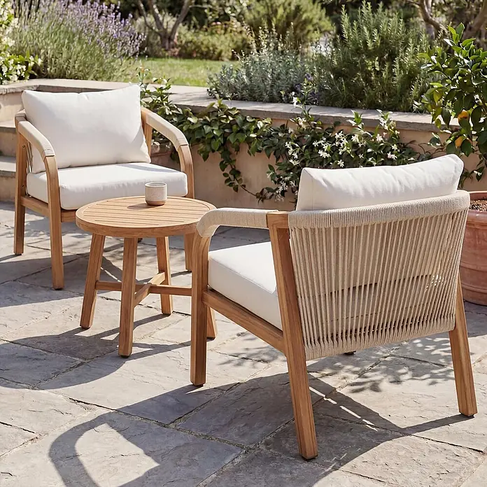 Mendler Aluminium Lounge-Set HWC-P82 Stoff/Textil - Holz-Optik creme -  - Zwei Holz-Terrassenstühle mit weißen Kissen und ein runder Holz-Beistelltisch auf einer Steinterrasse.