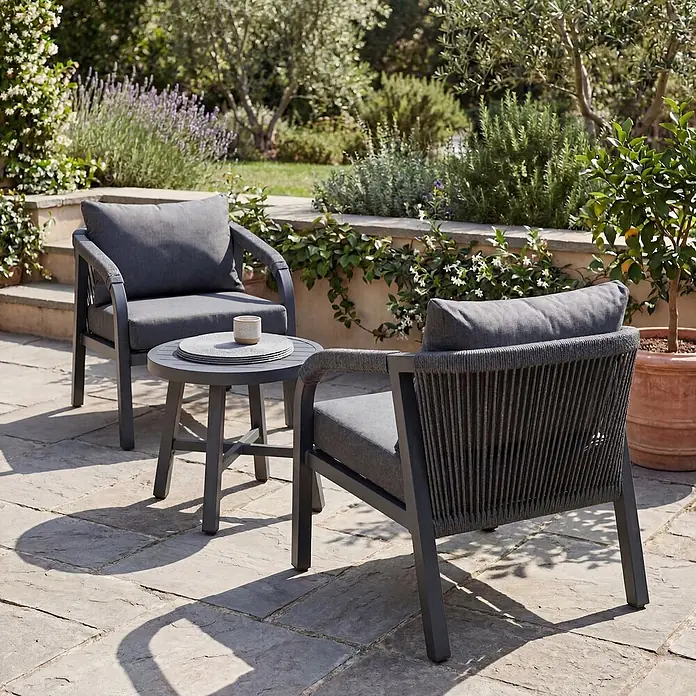 Mendler Loungemöbel-Set HWC-P82 - 3 -tlg., Metall, Dunkelgrau, Dunkelgrau - Zwei dunkelgraue Gartenstühle mit geflochtenen Seilakzenten und passendem Rundtisch auf einer Steinterrasse im Garten.