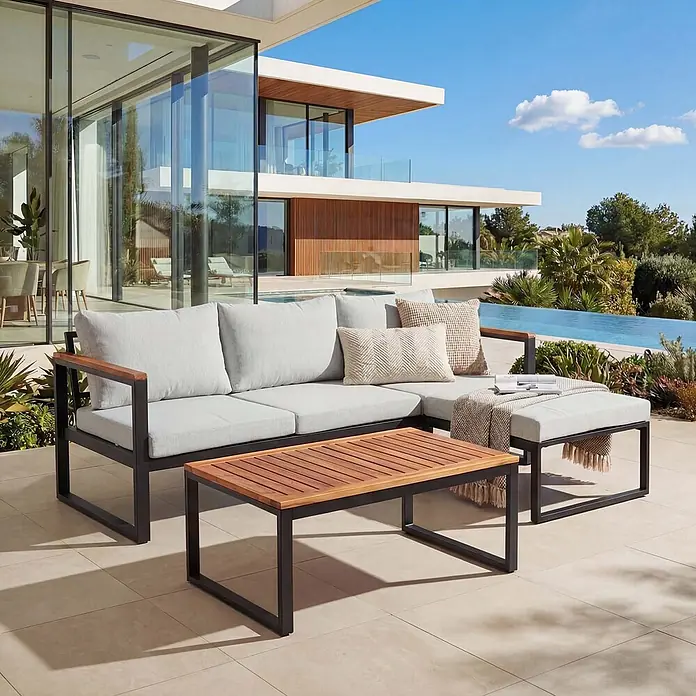 Mendler Loungemöbel-Set HWC-L26 - 3 -tlg., Textil, Hellgrau, Helllgrau - Ein Outdoor-Ecksofa mit hellgrauen Polstern, dunklem Metallrahmen und Holzdetails, dazu ein passender Couchtisch aus Holz auf einer Terrasse.