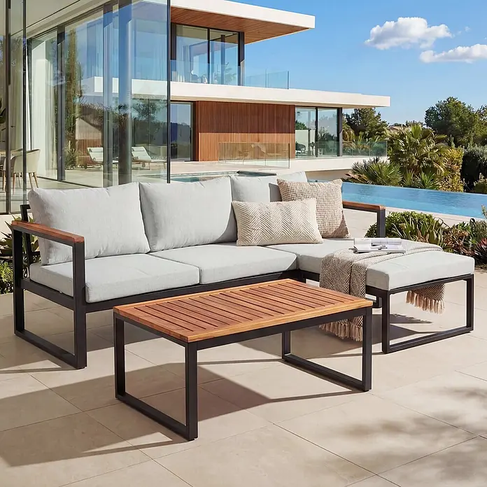 Mendler Loungemöbel-Set HWC-L26 - 3 -tlg., Textil, Hellgrau, Helllgrau - Moderne Outdoor-Lounge-Garnitur mit dunklen Metallrahmen, Holzdetails, hellgrauen Kissen, passendem Couchtisch und Ottoman auf einer Terrasse.