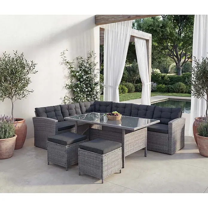 Mendler Loungemöbel-Set HWC-A29 - 5 -tlg., Polyrattan, Grau, Kissen grau + 2x Hocker, Grau - Graue Rattan-Ecksofa-Garnitur mit dunklen Kissen, Glastisch und zwei Hockern auf einer Terrasse.