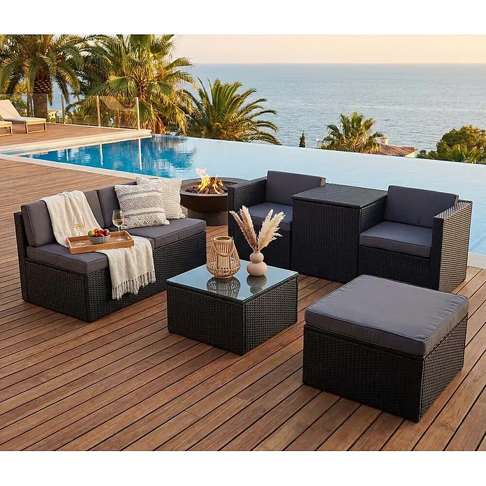 Mendler Loungemöbel-Set HWC-D21 - 7 -tlg., Polyrattan, Anthrazit, Kissen dunkelgrau, Anthrazit, grau - Eine schwarze Outdoor-Möbelgarnitur aus geflochtenem Rattan mit grauen Kissen und einem Couchtisch mit Glasplatte, am Pool mit Meerblick arrangiert.
