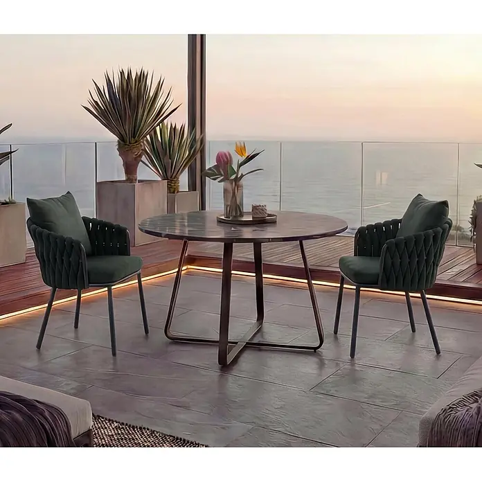 Mendler Gartenstuhl-Set HWC-P89 - 2 Stk., Metall, Grün, B x T x H: 56 x 57 x 71 cm - Zwei dunkelgrüne Samtstühle mit geflochtenen Rückenlehnen und ein runder Tisch auf einer Terrasse mit Meerblick bei Sonnenuntergang.