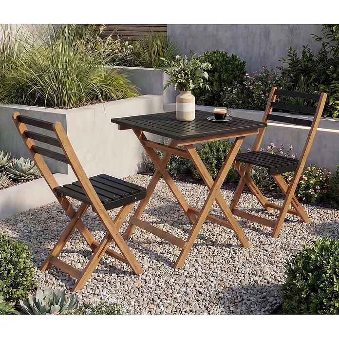 Mendler Garnitur HWC-P71 Akazie Holz klappbar - Natur-schwarz -  - Kompaktes Bistro-Set für den Außenbereich mit Naturholzrahmen und schwarz-lamelliertem Tisch und Stühlen auf einem Kieshof.