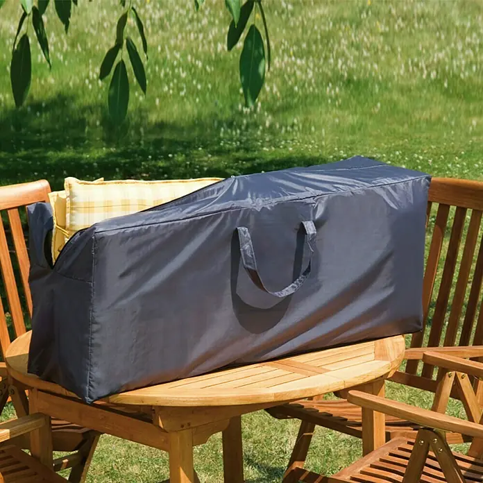 Sunfun Auflagen-Schutzhülle - L x B x H: 125 x 32 x 50 cm, Polyester, 160 g/m², Schwarz - Eine graue Schutzhülle mit Griffen liegt auf einem Holztisch im Freien und schützt möglicherweise Gartenmöbel oder Kissen.