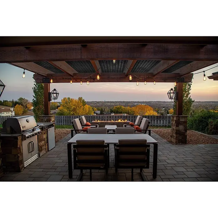 Malla sombreadora - L x Al: 10 x 2 m, Negro, Polietileno - Patio exterior bajo pérgola de madera, iluminado con luces de cadena, con zona de comedor, sillones, parrilla y fogata, con vista al atardecer.