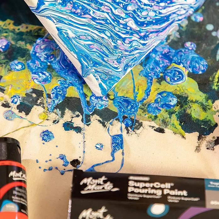 Mont Marte Acrylfarben-Set SuperCell® Tropical Ocean - mehrfarbig, 4 Stk. x 60 ml, Flasche - Flasche und Karton Mont Marte SuperCell Pouring Paint bei einem Acryl-Pouring-Kunstprojekt, blaue Farbe tropft von einer Leinwand.