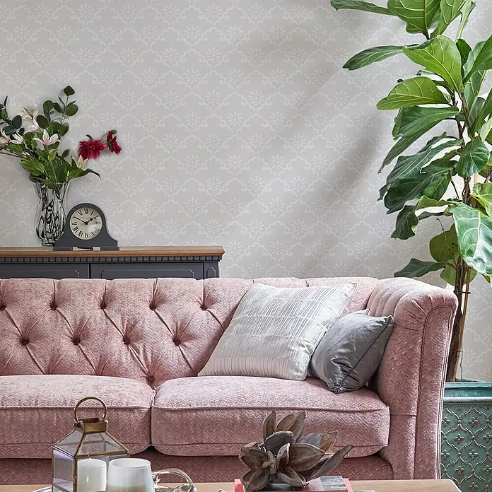 Vliestapete Laura Ashley Coralie  1000x52cm -  - Ein rosafarbenes getuftetes Sofa mit Kissen in einem gemütlichen Wohnzimmer.