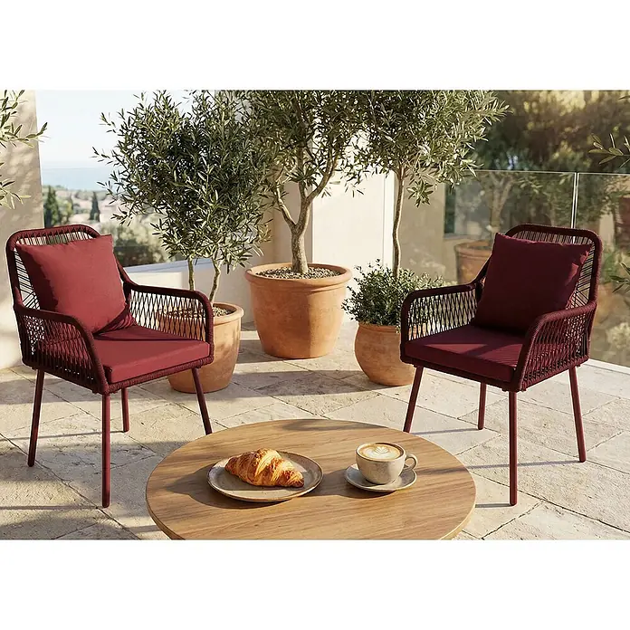 Mendler 2x Gartenstuhl HWC-O12 Rückenpolster - bordeaux, Bezug bordeaux -  - Zwei rote Outdoor-Stühle mit Geflechtdetails und Kissen, flankieren einen Holztisch mit Frühstück auf einer Terrasse.