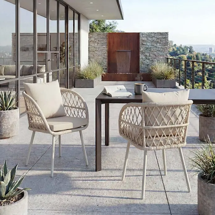 Mendler 2er-Set Gartenstuhl HWC-Q38 - Gestell hellgrau, Polster Creme -  - Zwei beigefarbene geflochtene Outdoor-Stühle mit Kissen stehen an einem dunklen Tisch auf einer Terrasse, bereit zum Essen oder Entspannen.