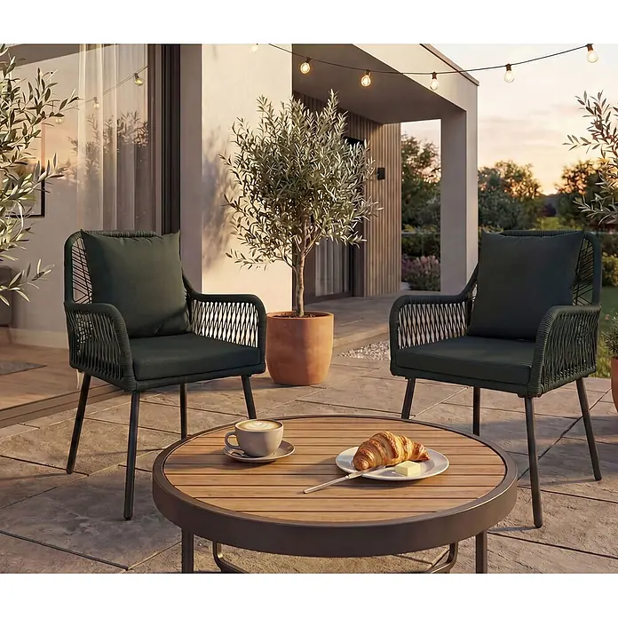 Mendler 2x Gartenstuhl HWC-O12 Rückenpolster - grün, Bezug grün -  - Zwei dunkelgrüne Outdoor-Stühle mit geflochtenen Lehnen und Kissen sowie ein runder Holztisch auf einer Terrasse.