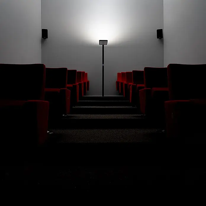 LUXULA LED Stehleuchte 100 W 4000 K neutralweiß schwarz dimmbar -  - Schlanke, schwarze Stehleuchte mit Rollstuhlsymbol beleuchtet Kinosaal mit roten Sitzen.