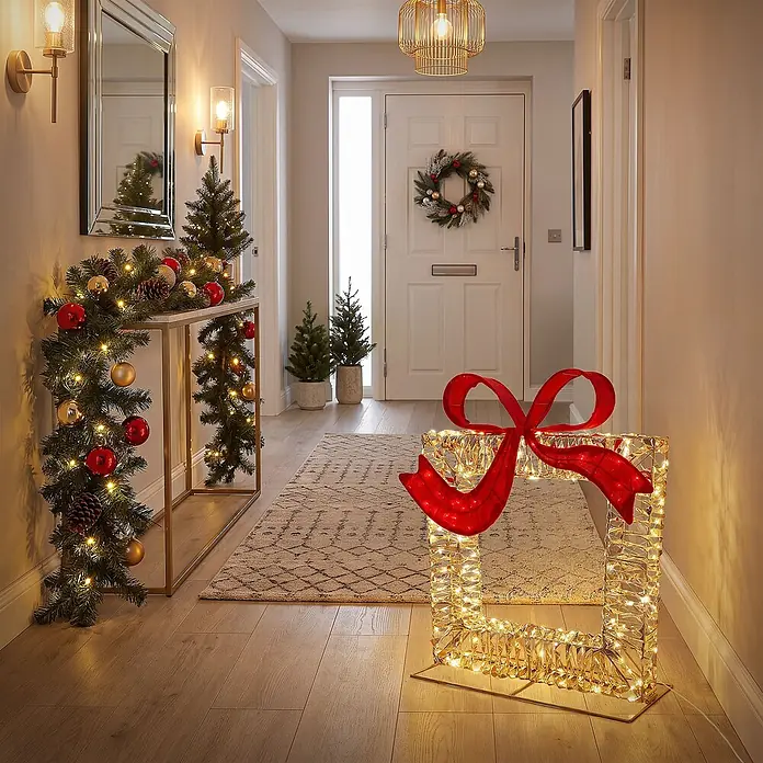 ECD Germany LED Geschenkbox Weihnachten mit Schleife, Weihnachtsdeko -  - Beleuchtete Weihnachtsgeschenkbox-Dekoration mit goldenem Drahtrahmen und großer roter Schleife, auf einem Flurboden.