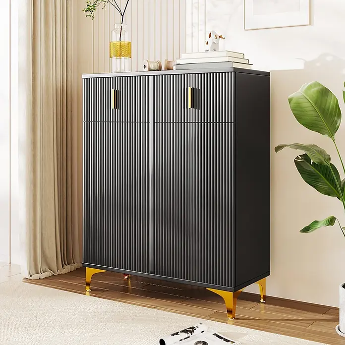 SONNENH Kommode - Schwarz, Anzahl Schubladen: 2 Stk. - Ein modernes dunkelgraues Sideboard mit geriffelten Türen, goldenen Griffen und Beinen, dekoriert mit Büchern, steht neben einem Vorhang und einer Pflanze.