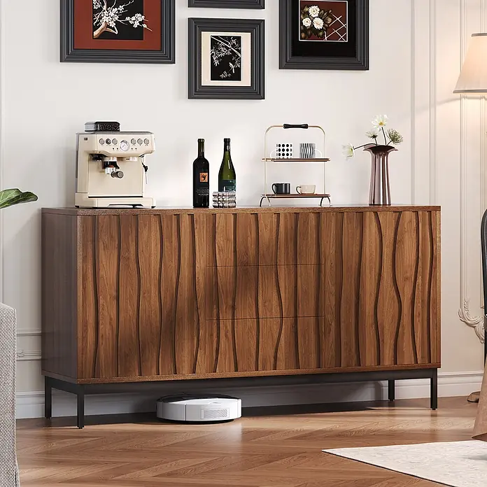 SONNENH Kommode - Dunkelbraun, Anzahl Schubladen: 3 Stk. - Dunkles Holz-Sideboard mit wellenförmigen Fronten und schwarzen Beinen, als Kaffeebar und Ablage im Wohnzimmer genutzt. Ein Saugroboter ist darunter.