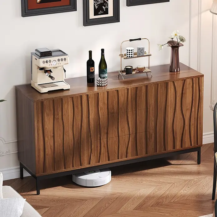 SONNENH Kommode - Dunkelbraun, Anzahl Schubladen: 3 Stk. - Dunkles Holz-Sideboard mit gewellter Front und schwarzen Beinen, zeigt Kaffeemaschine und Deko. Roboterstaubsauger darunter.