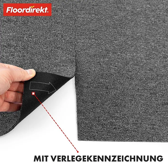 Floordirekt Teppichfliese Moscow 50 x 50 cm Dunkelgrau -  - Hand zieht dunklen grauen Floordirekt Teppichfliesenrand hoch, zeigt weiße Kleberückseite mit Verlegerichtungspfeil.