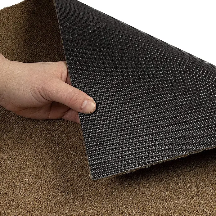 Floordirekt Teppichfliese Edinburgh - 50 x 50 cm - 0,25 m² - Beige -  - Eine Hand hebt eine braune Textilmatte an und enthüllt ihre schwarze, genoppte Anti-Rutsch-Rückseite.