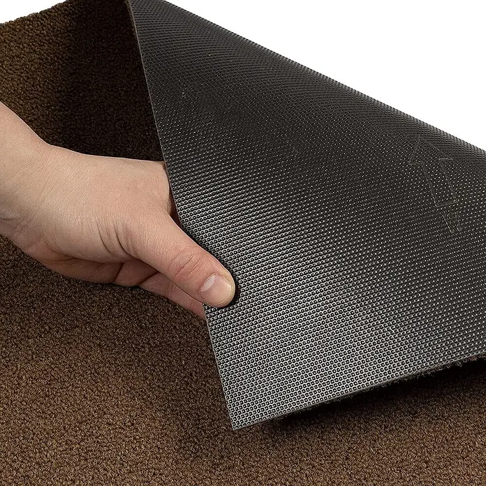 Floordirekt Teppichfliese Edinburgh - 50 x 50 cm - 0,25 m² - Braun -  - Eine Hand hebt eine braune Matte an und zeigt ihre strukturierte schwarze Anti-Rutsch-Unterseite.