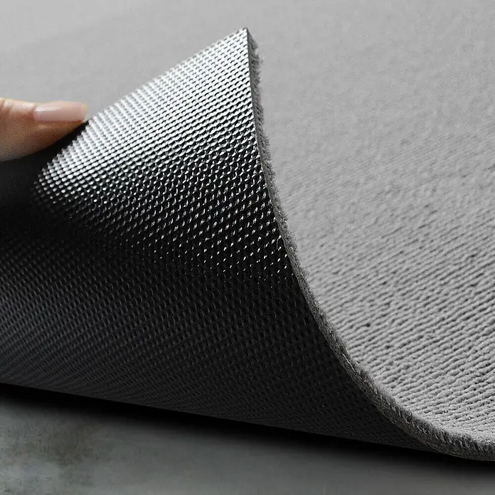 Floordirekt Teppichfliese Lyonn - 50 x 50 cm - 0,25 m² - Hellgrau -  - Eine graue Matte angehoben, um ihre weiche Oberfläche und die dunkle, strukturierte Anti-Rutsch-Unterseite zu zeigen.