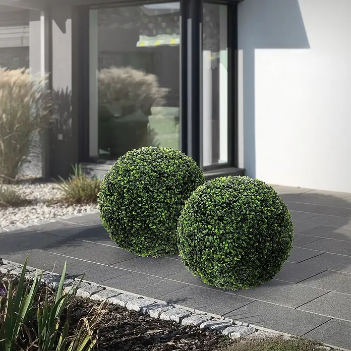 2er Set Künstliche Buchsbaumkugel groß Ø35 cm Grün aus Kunststoff -  - Zwei grüne künstliche Buchsbaumkugeln auf einem gepflasterten Weg vor einem modernen Haus als Outdoor-Dekoration.