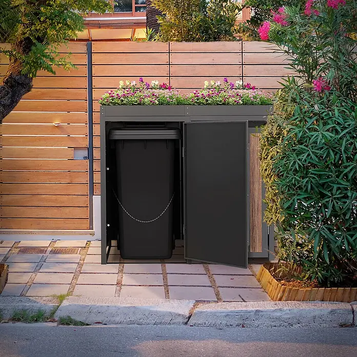 ML-Design Mülltonnenbox 2er 240L mit Pflanzdach Anthrazit-Holzoptik -  - Dunkelgraue Mülltonnenbox mit integriertem Pflanzkasten, eine Tür offen, die einen schwarzen Mülleimer zeigt, draußen neben einem Holzzaun.