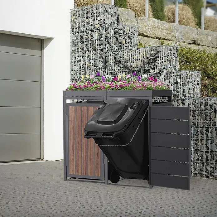ML-Design Mülltonnenbox 2er 240L mit Pflanzdach Anthrazit-Holzoptik -  - Dunkelgraue Mülltonnenbox mit Holzpaneel und bepflanzter Oberseite, zeigt eine gekippte schwarze Mülltonne.