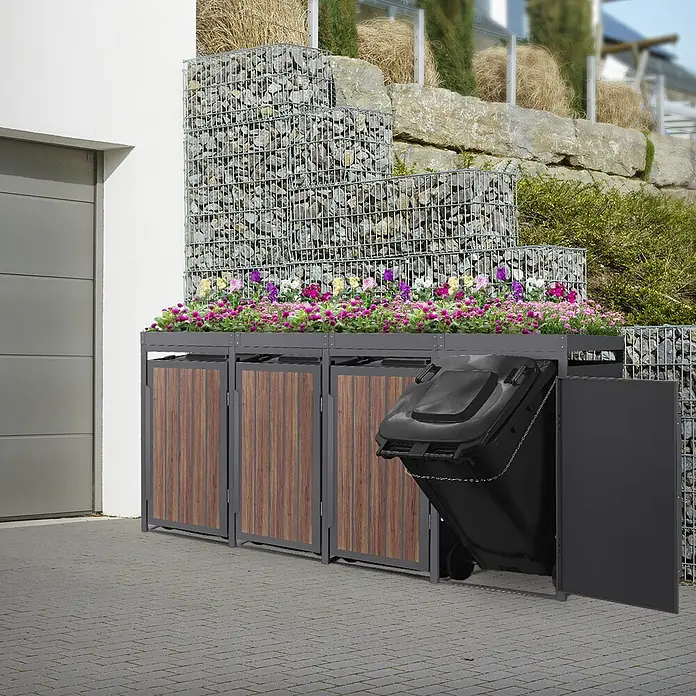 ML-Design Mülltonnenbox 4er 240L Pflanzdach 260x80x124 Anthrazit-Holzoptik -  - Mülltonnenbox für draußen mit dunkelgrauem Rahmen, Holzoptik-Türen und Blumenbeet, neben Garage, eine Tonne ausgezogen.