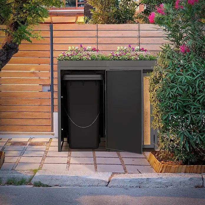 ML-Design Mülltonnenbox 2er 240L Pflanzdach Anthrazit-Holzoptik -  - Dunkelgraue Mülltonnenbox mit Blumenbeet oben, offener Tür, die eine schwarze Mülltonne zeigt, neben einem Holzzaun im Freien.
