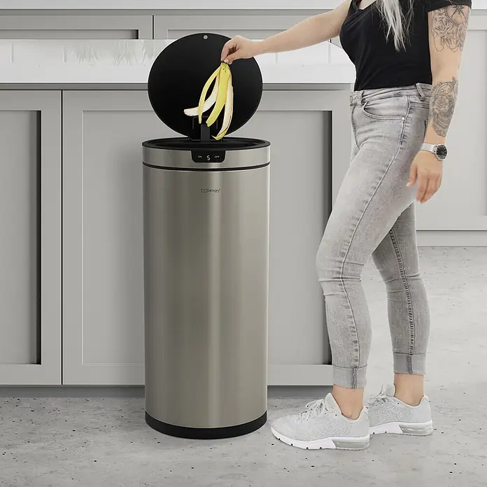 Mülleimer mit Sensor 40L rund aus Edelstahl, Silber, Automatisch -  - Eine Person entsorgt Bananenschalen in einem hohen, automatischen Abfalleimer aus Edelstahl mit offenem Deckel.