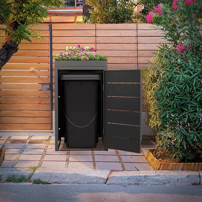 Mülltonnenbox 1er mit Pflanzdach 240L 68x80x124 cm Anthrazit aus Stahl -  - Dunkelgraue Mülltonnenbox mit integriertem Pflanzgefäß, geöffnet, um eine schwarze Tonne zu zeigen, draußen auf einem gepflasterten Weg.