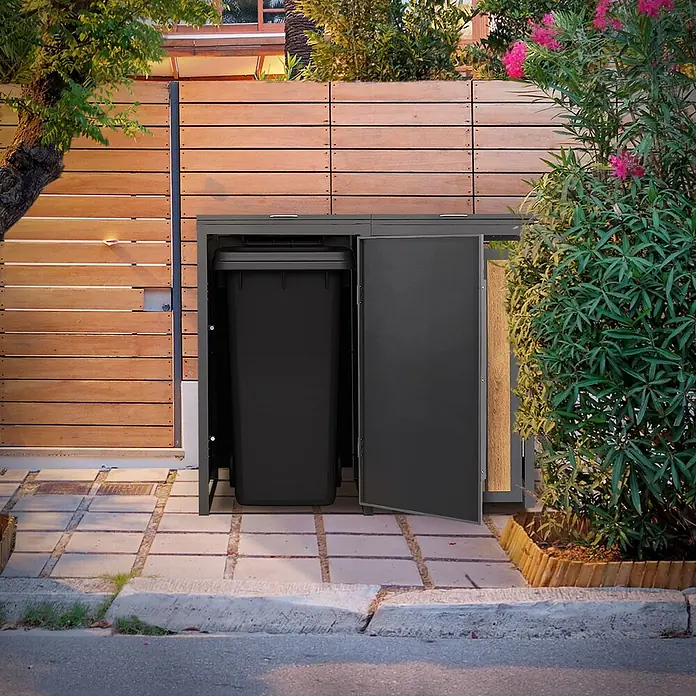 ML-Design Mülltonnenbox 2er 240L 132x80x120 cm Anthrazit-Holzoptik Müllbox -  - Dunkelgraue Mülltonnenbox mit offener Tür, die eine schwarze Tonne zeigt, neben einem Holzzaun und Pflanzen.
