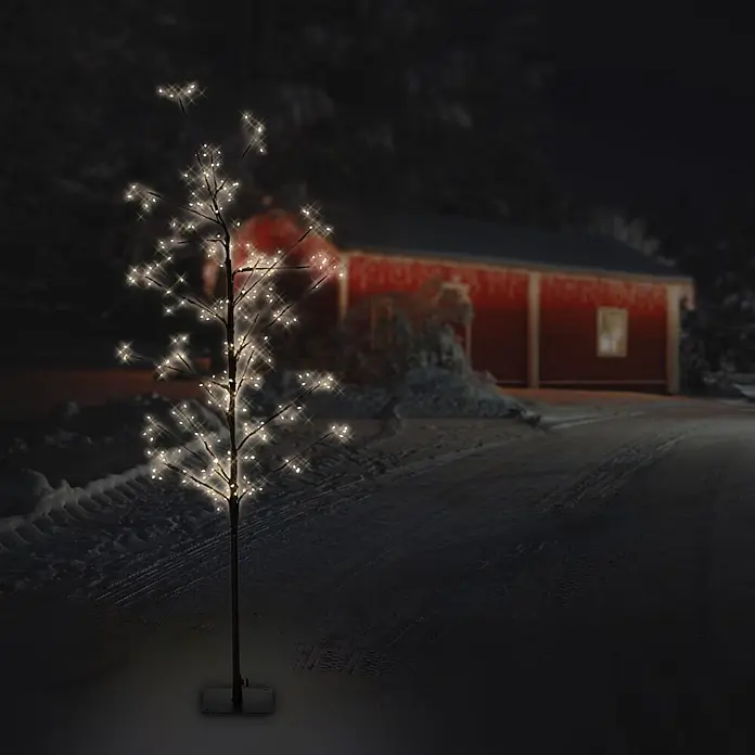 LED-Baum 120 cm 240LED Warmweiß Timer Außen Flexibel Zweige -  - Beleuchteter Dekorationsbaum mit warmweißen LEDs an dunklen Ästen, auf verschneitem Weg bei Nacht vor rotem Gebäude.