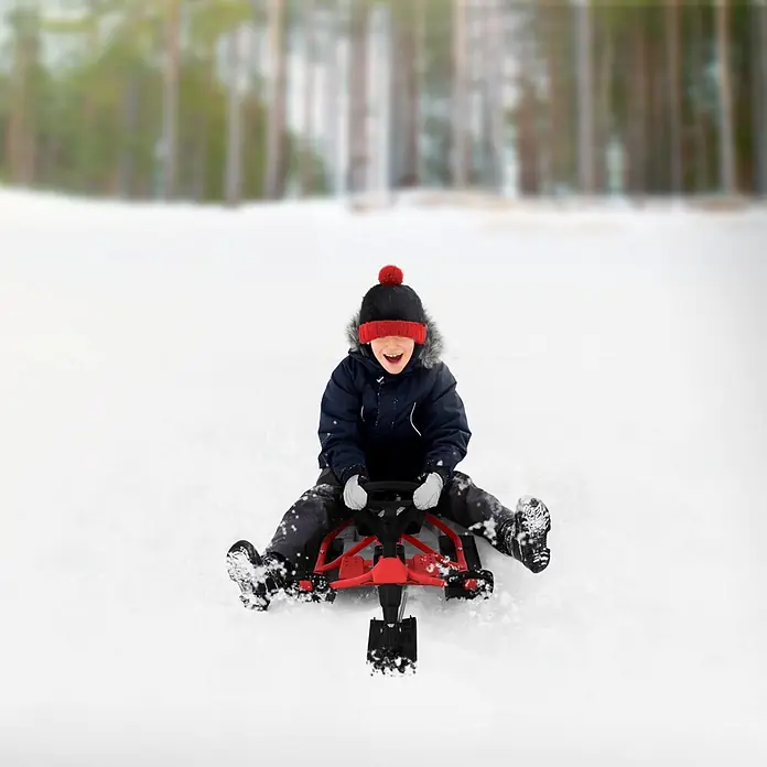 Lenkschlitten für Kinder Rot 119 x 38 x 50 cm Stahlrahmen bis 90 kg -  - Kind auf einem rot-schwarzen Schneeschlitten, lachend im Schnee fahrend.