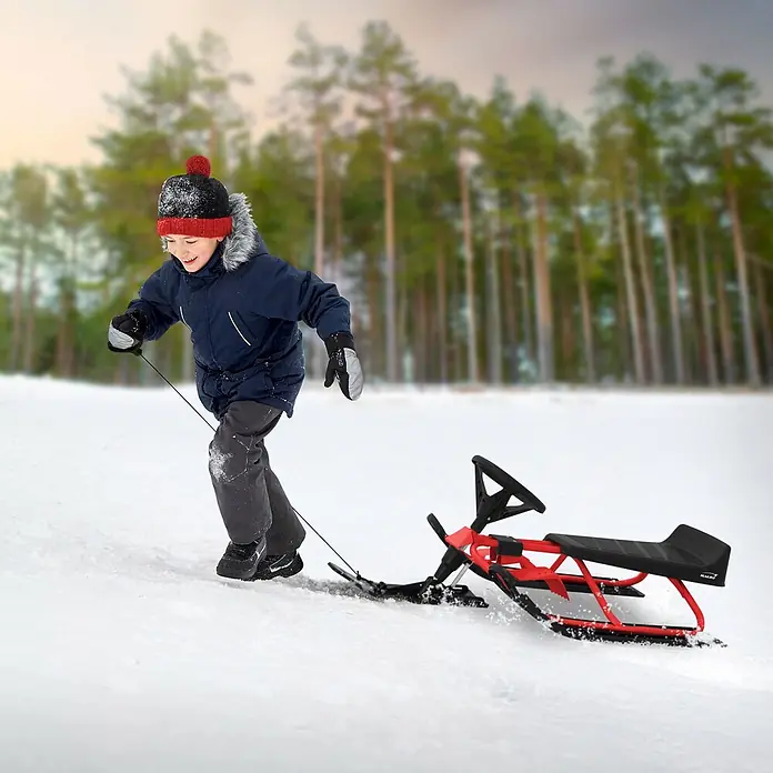 Lenkschlitten für Kinder Rot 119 x 38 x 50 cm Stahlrahmen bis 90 kg -  - Ein Kind zieht einen roten und schwarzen Lenkschlitten mit Lenkrad einen verschneiten Hügel hinauf.