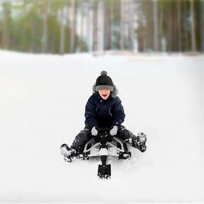 Lenkschlitten für Kinder Weiß 119 x 38 x 50 cm Stahlrahmen bis 90 kg -  - Kind in Winterkleidung fährt fröhlich auf einem schwarz-weißen Schneeschlitten einen verschneiten Hang hinunter.